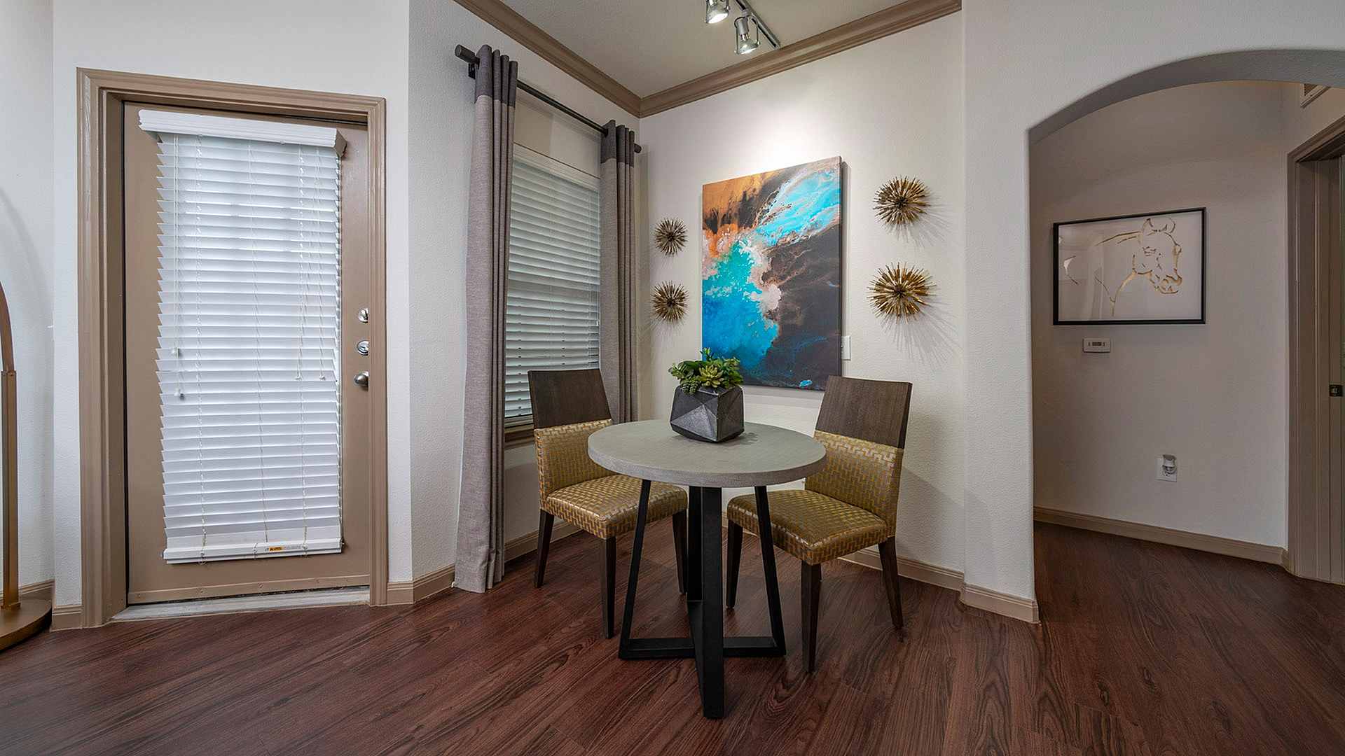 Chic dining nook with modern artwork, featuring a round table and stylish chairs on elegant hardwood floors.