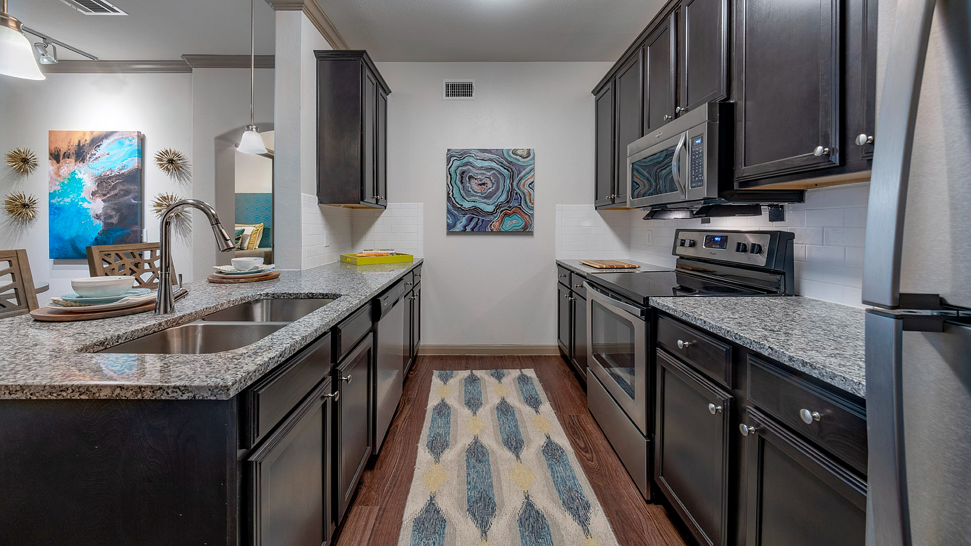 Modern kitchen with sleek granite countertops and stainless steel appliances, enhanced by chic dark cabinetry and elegant decor.