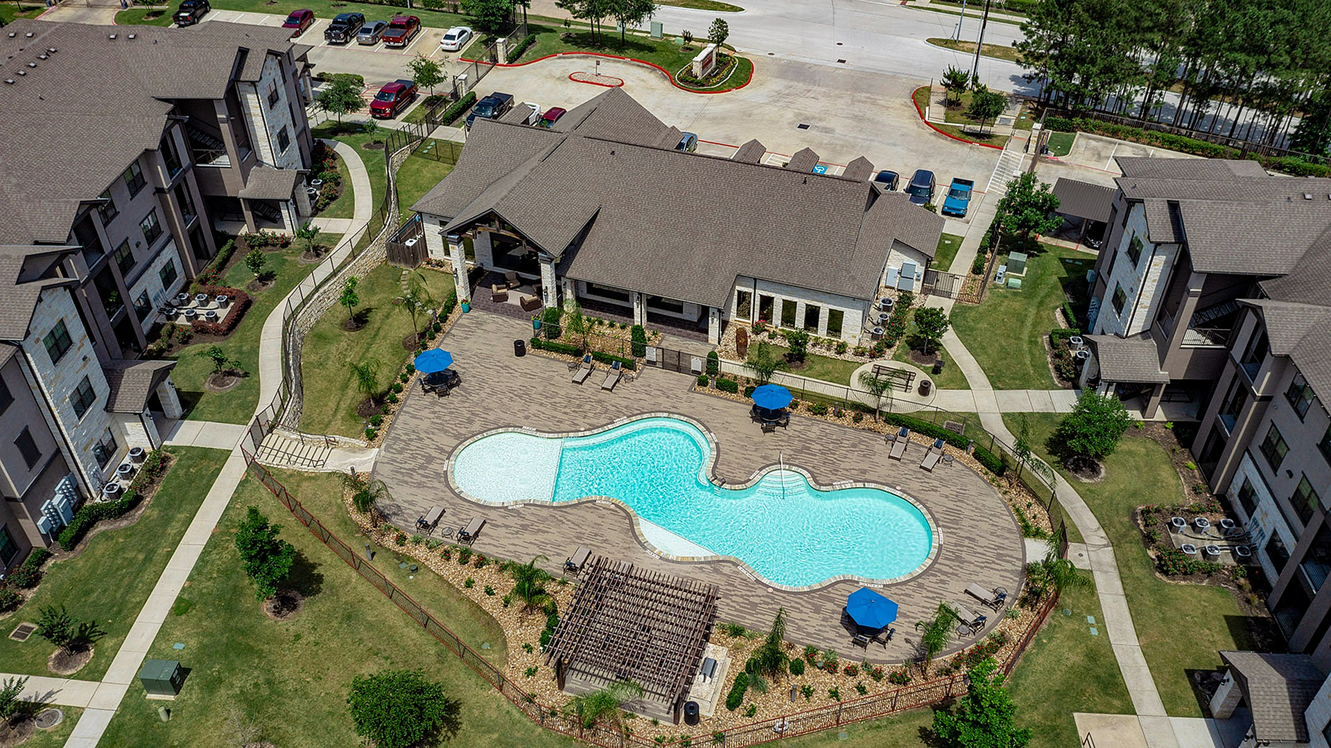 Aerial view of a luxurious apartment complex with a stunning resort-style pool, surrounded by lush greenery and modern buildings.