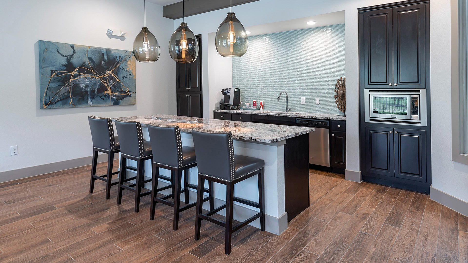 Chic modern kitchen featuring sleek granite countertops, elegant pendant lighting, and stylish bar seating with a contemporary art accent.