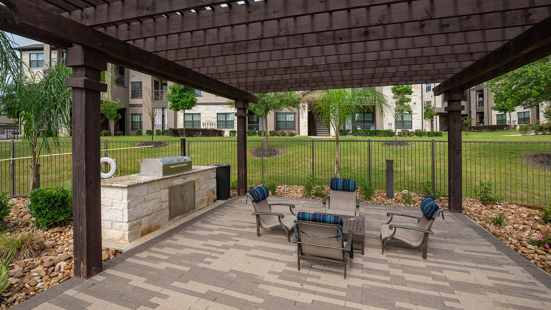 Charming outdoor seating area with a pergola and built-in grill, set in a lush garden courtyard.