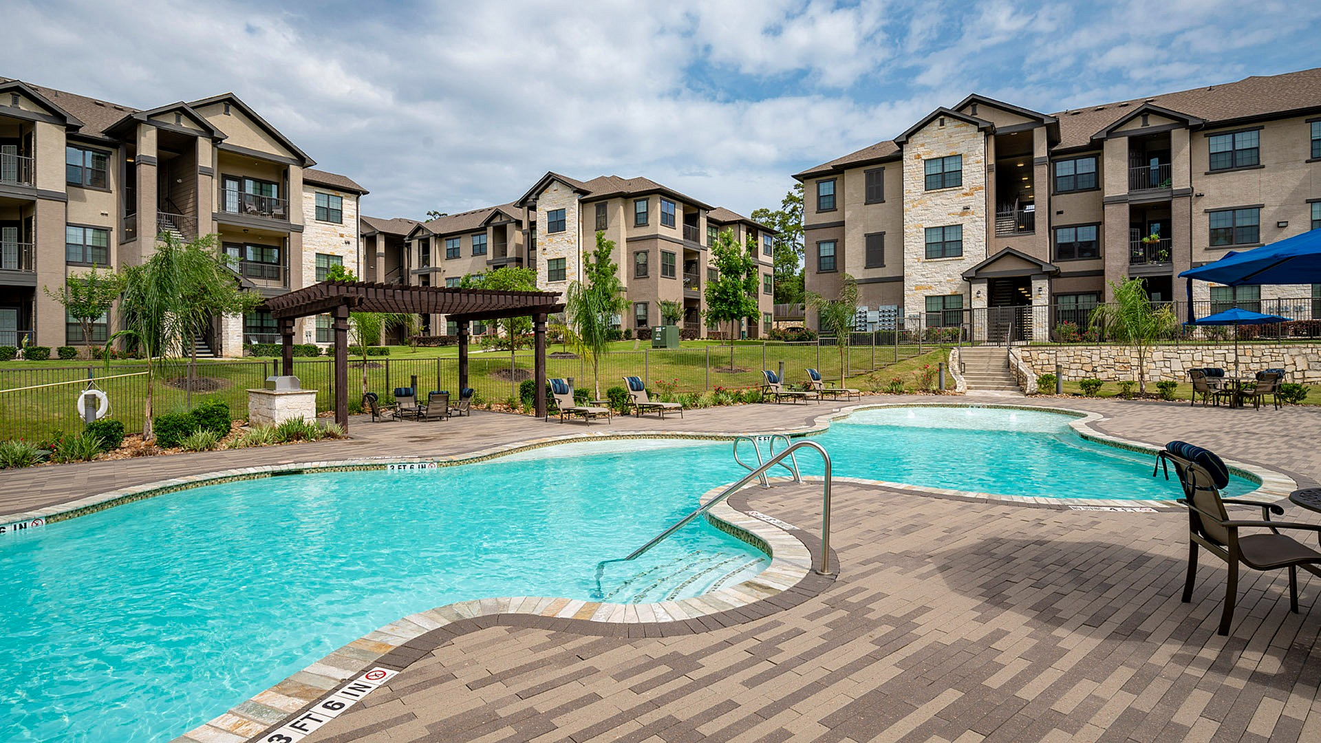 Luxurious apartment complex with a sparkling outdoor pool, modern patio seating, and lush greenery, perfect for relaxation and recreation.