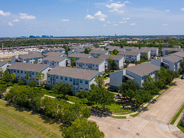 Aerial of apartment community, tree-lined streets and city skyline, Houston, TX