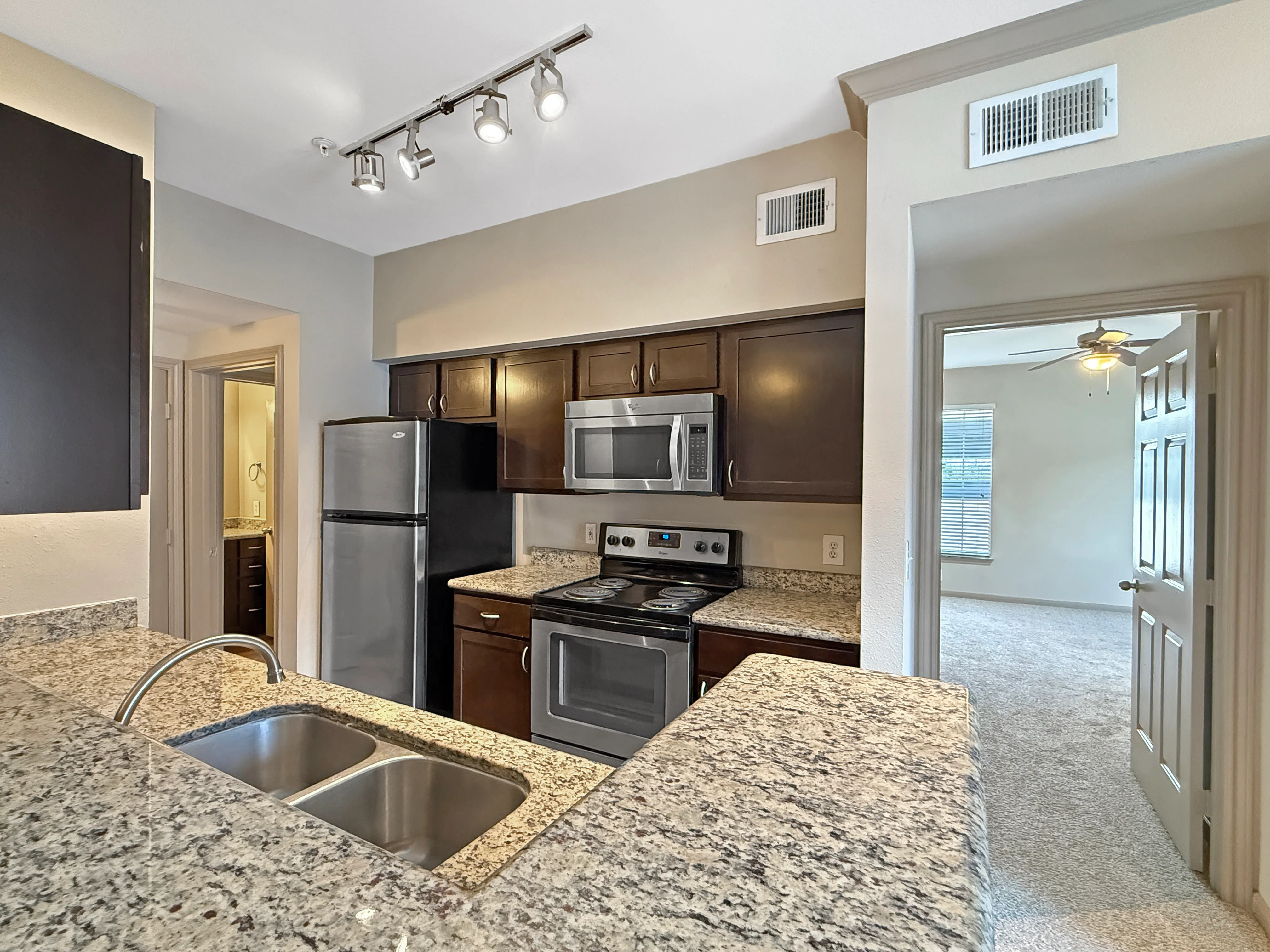 Chic apartment kitchen with granite countertops, stainless steel appliances, and dark wood cabinetry, adjacent to a spacious living area.
