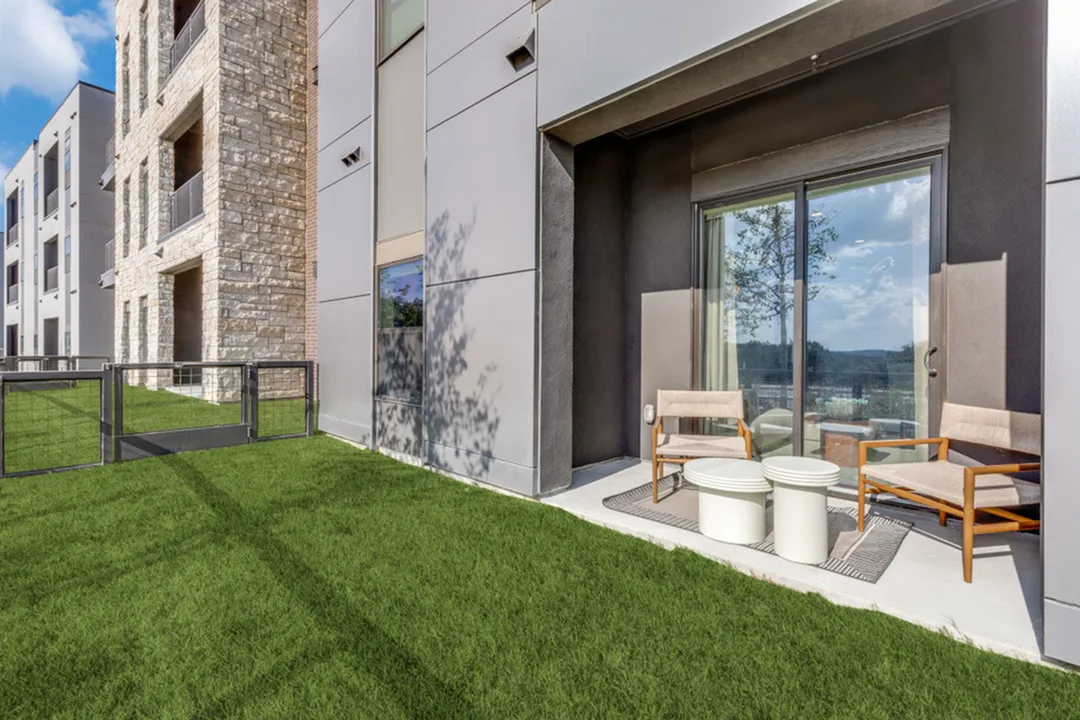 Chic apartment patio featuring lush green grass and cozy outdoor seating, perfect for relaxation and entertaining.
