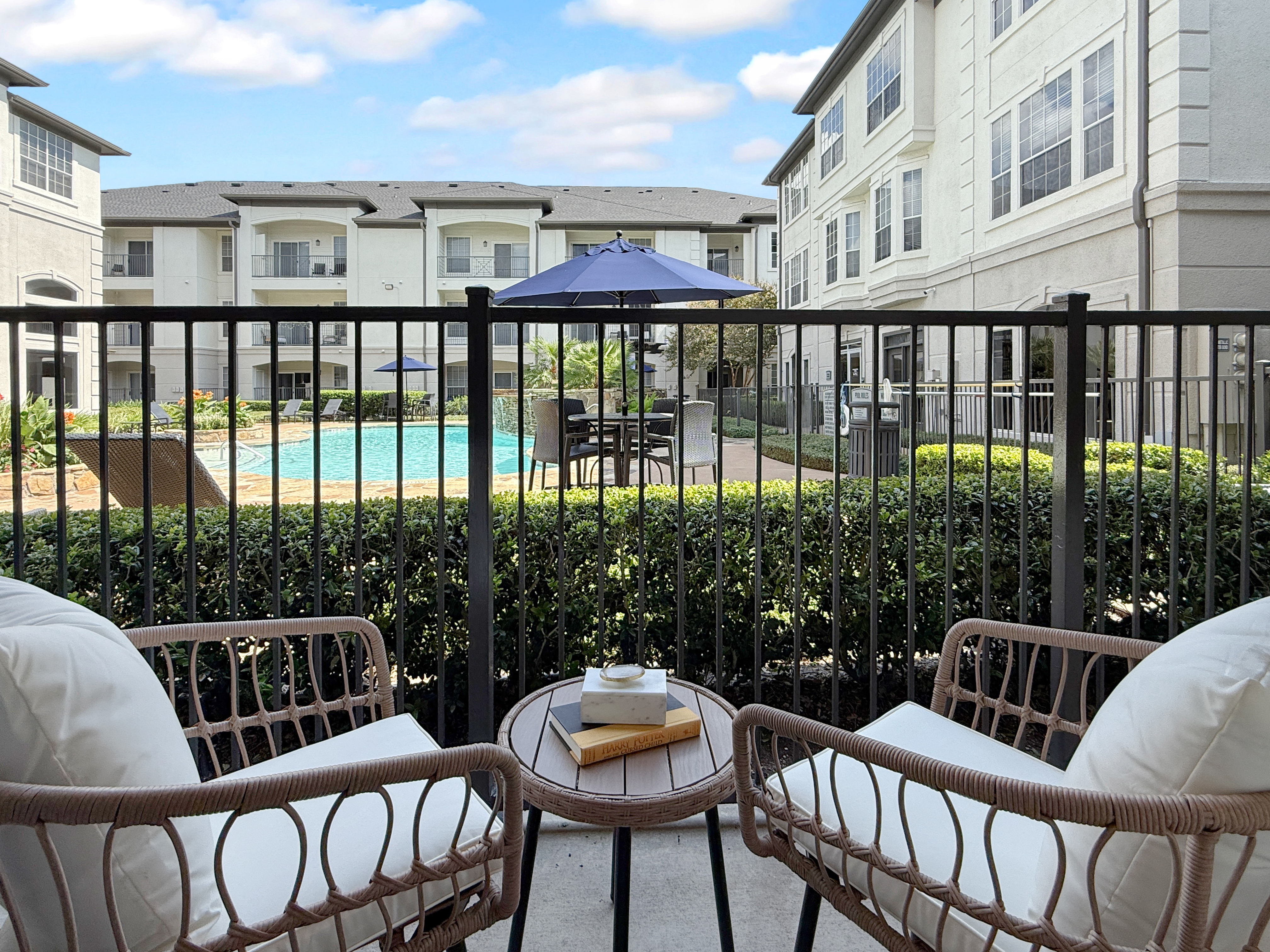 Charming apartment balcony with cozy seating, overlooking a serene pool area and elegant modern architecture, perfect for relaxation and leisure.