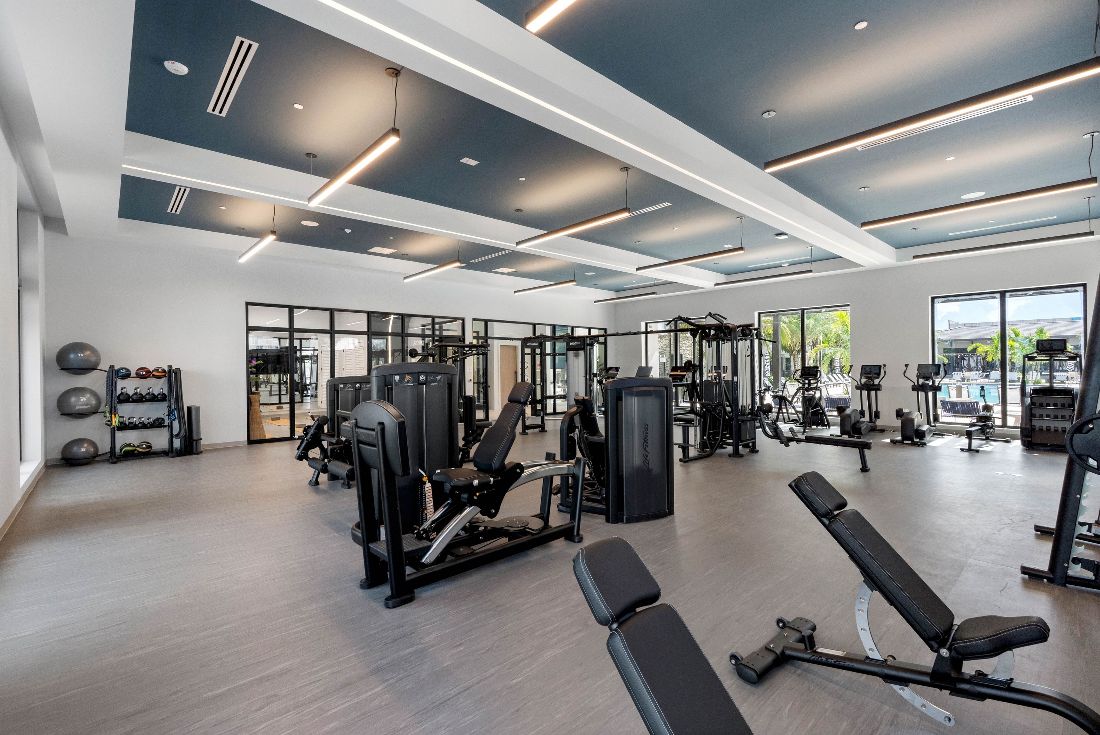 Modern apartment building gym with sleek exercise equipment, large windows, and ample natural light.