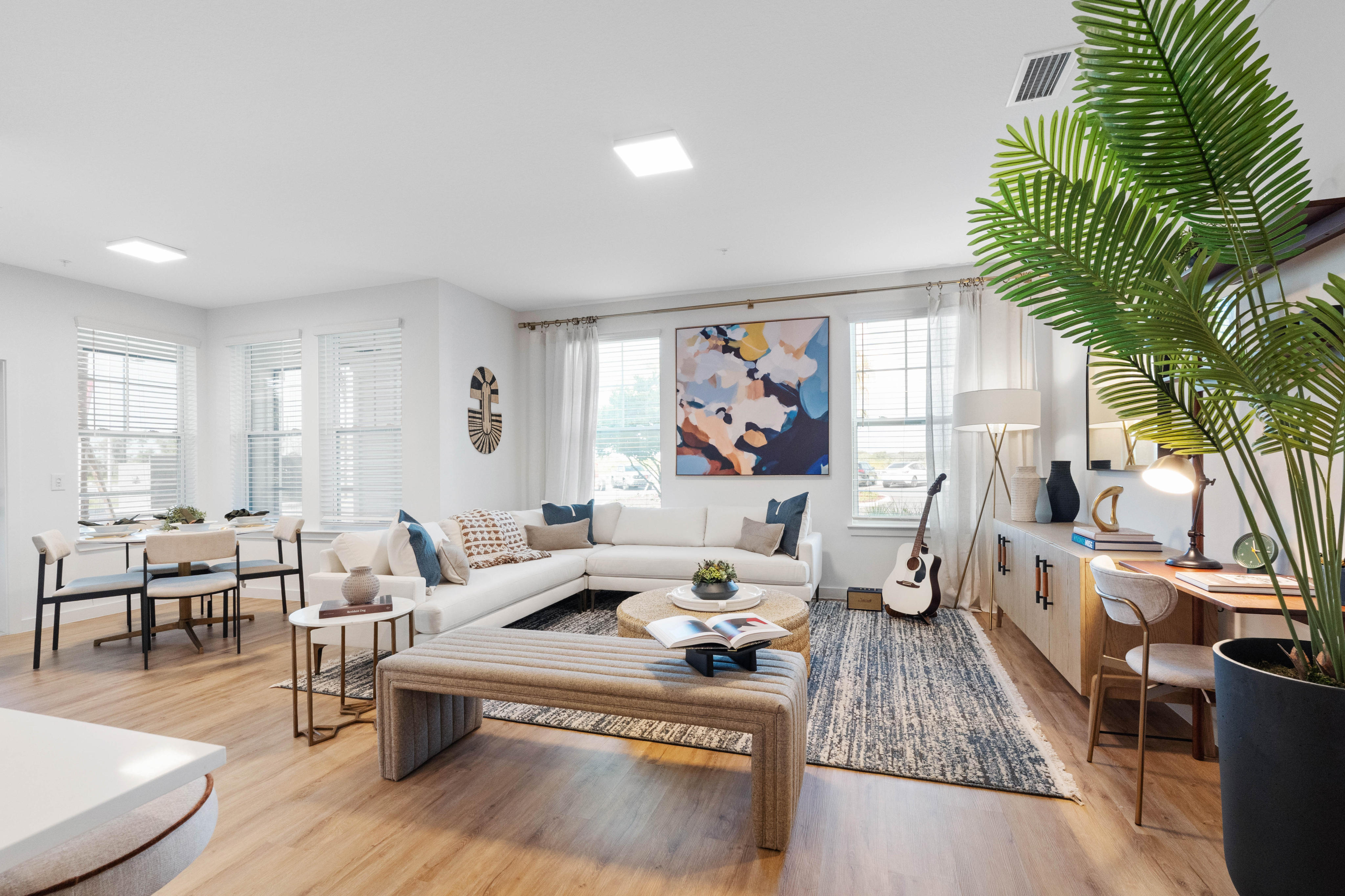 Chic and bright living area featuring a cozy sectional sofa, modern art piece, elegant dining setup, and stylish decor with abundant natural light.