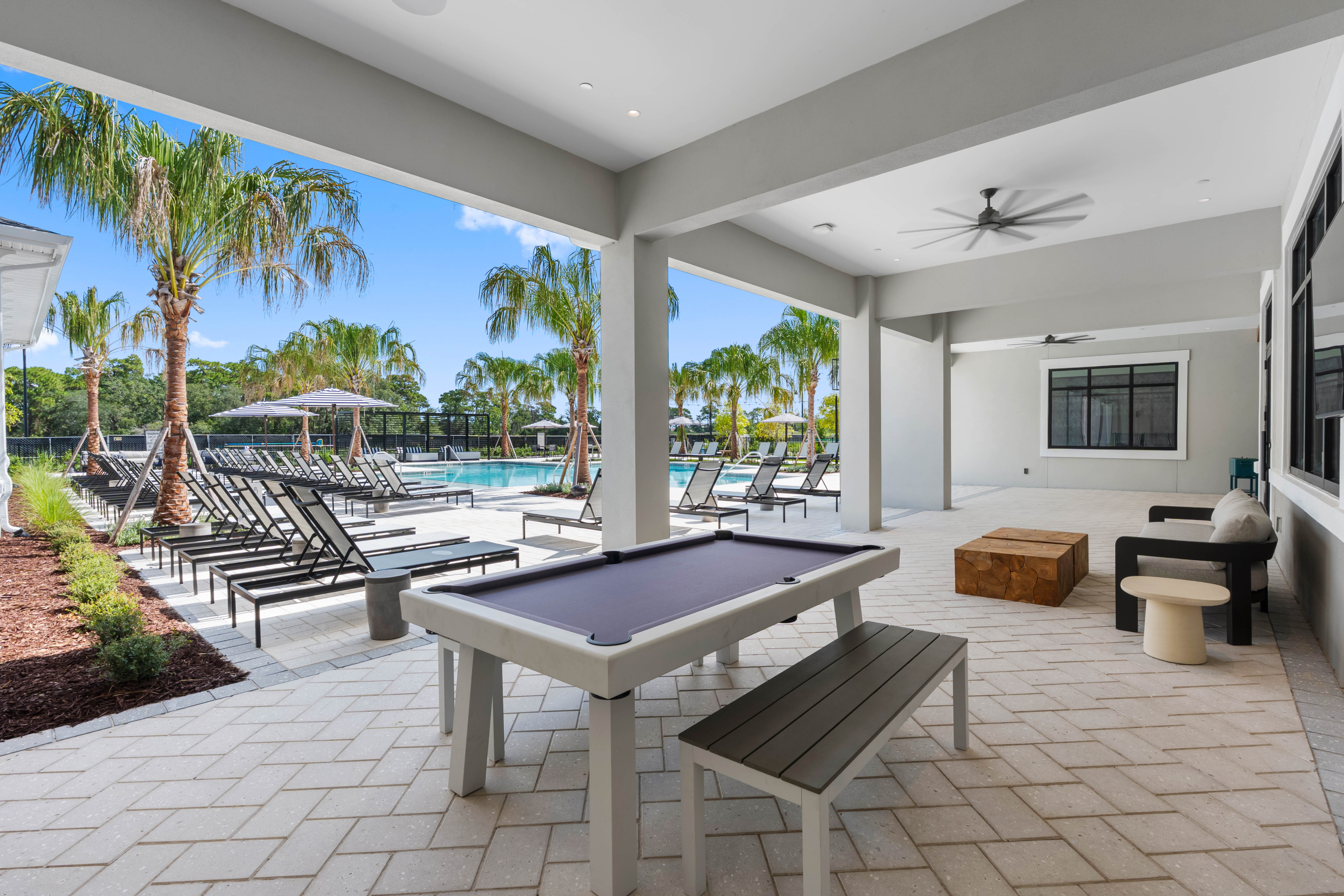 Luxurious outdoor patio with stylish seating, billiards table, and a view of the inviting pool area surrounded by palm trees.