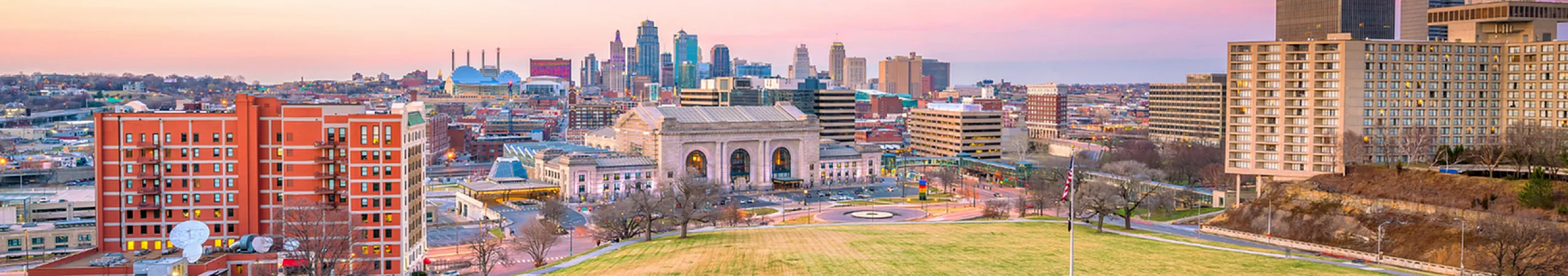 Panoramic view of a vibrant city skyline during a colorful sunset, highlighting modern architecture and urban green spaces.