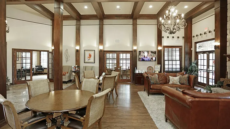 Luxurious communal lounge with rich wood beams, plush leather sofas, and a grand chandelier, offering a warm and inviting atmosphere.