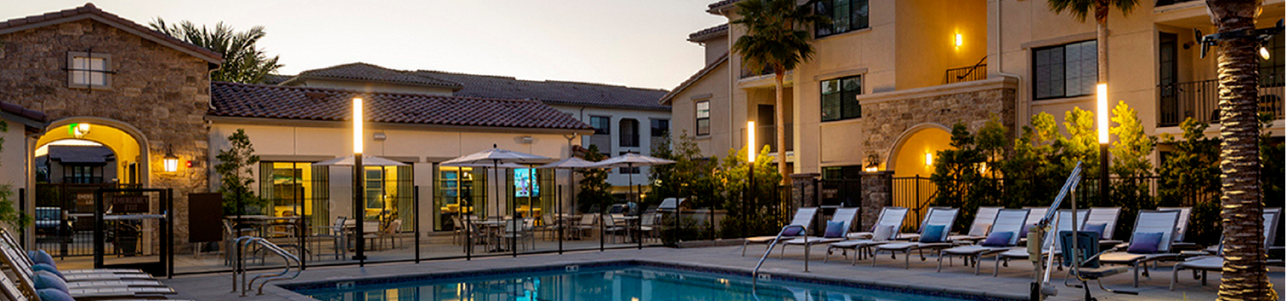 Inviting evening view of a luxury apartment complex pool surrounded by palm trees and modern architecture.