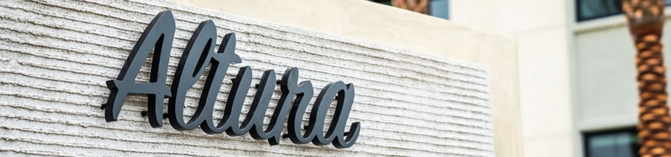 Entrance sign of Altura The Groves featuring modern typography set against a textured backdrop with palm trees in view.