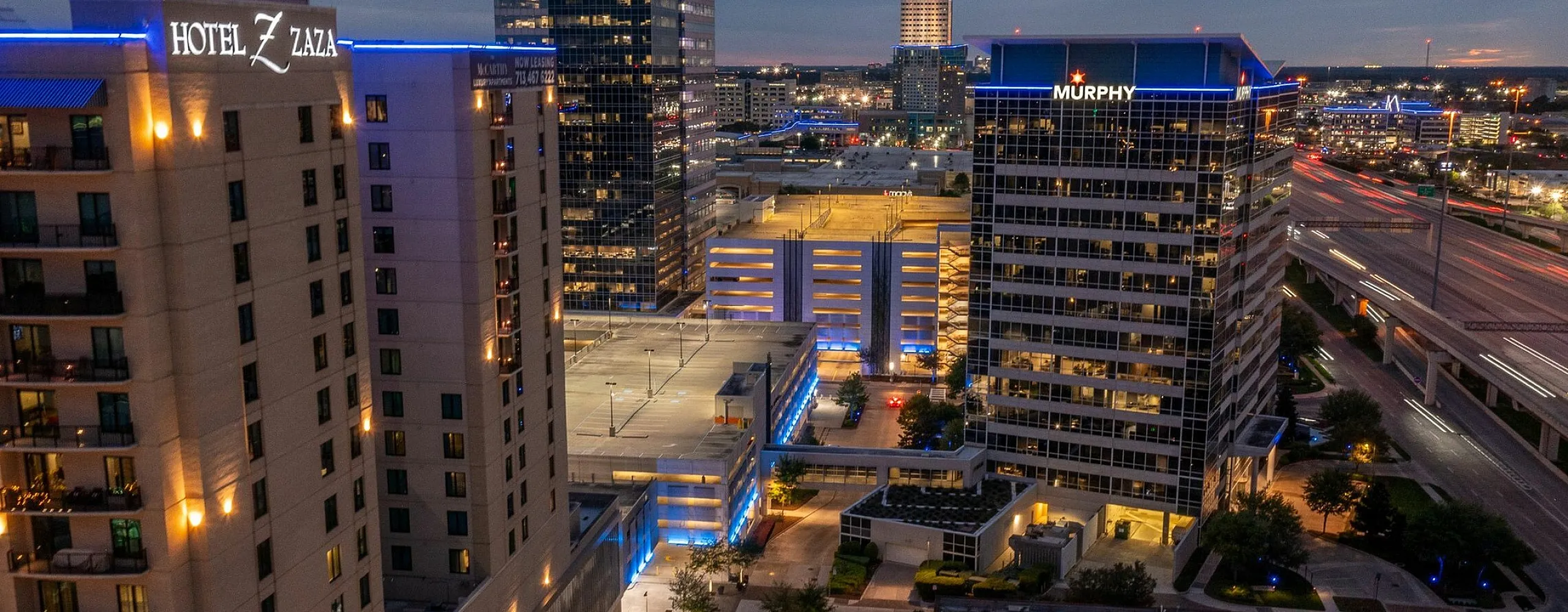 Aerial view of a bustling cityscape at night, featuring illuminated skyscrapers and busy streets.