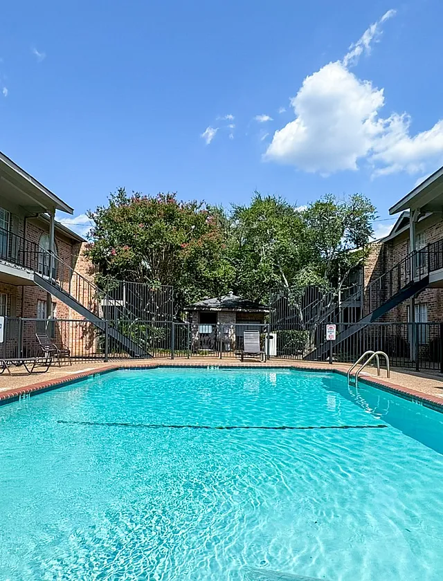 Inviting apartment complex courtyard featuring a large sparkling pool framed by classic brick buildings.