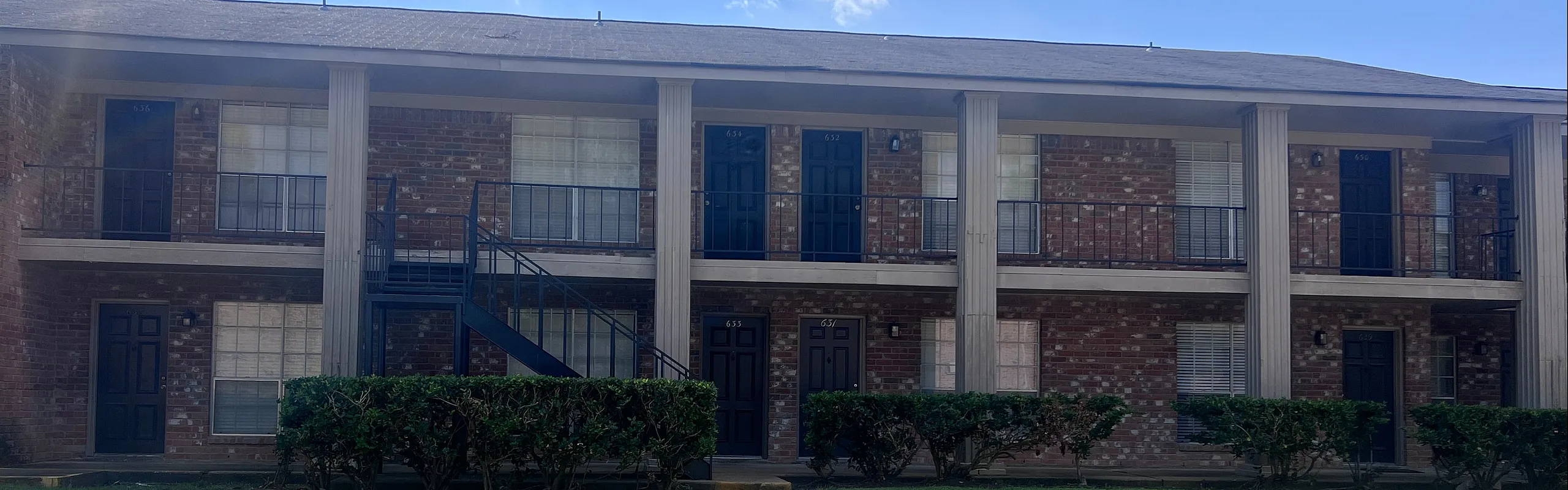 Lovely two-story brick apartment building with balconies and lush green surroundings.