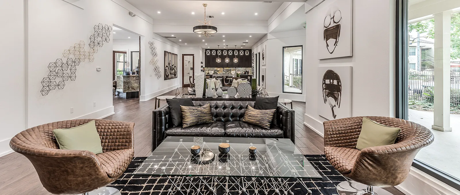 Chic living area with modern design, featuring a sleek black leather couch, artistic décor, and abundant natural light from large windows.