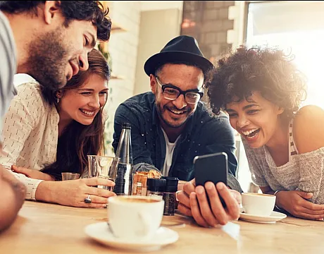 Vibrant group of friends enjoying coffee and laughter at a cozy cafe, sharing moments over a smartphone.