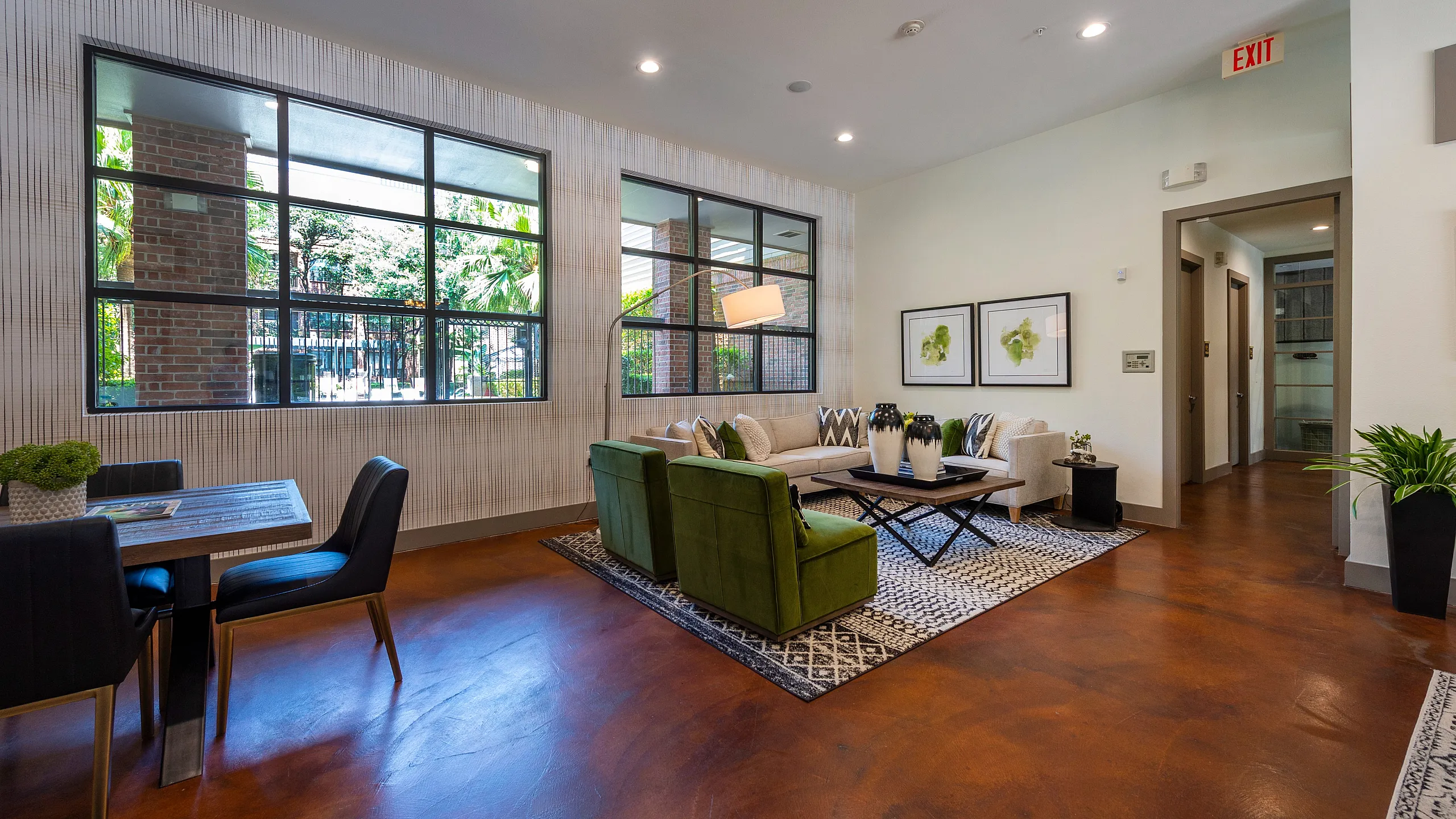 Chic modern living area with green velvet chairs, cozy sofa, and stylish decor, filled with natural light from large windows.