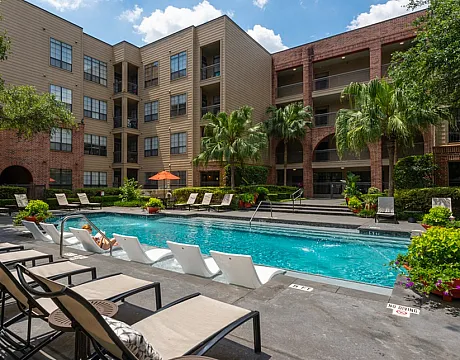 Luxurious apartment complex featuring a resort-style pool area with stylish loungers, surrounded by lush greenery and modern architecture.