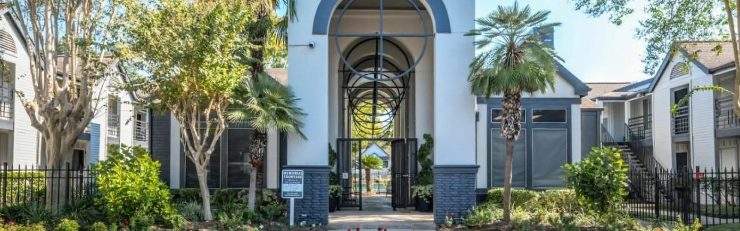 Elegant apartment entrance with modern architecture surrounded by lush greenery and vibrant palm trees.
