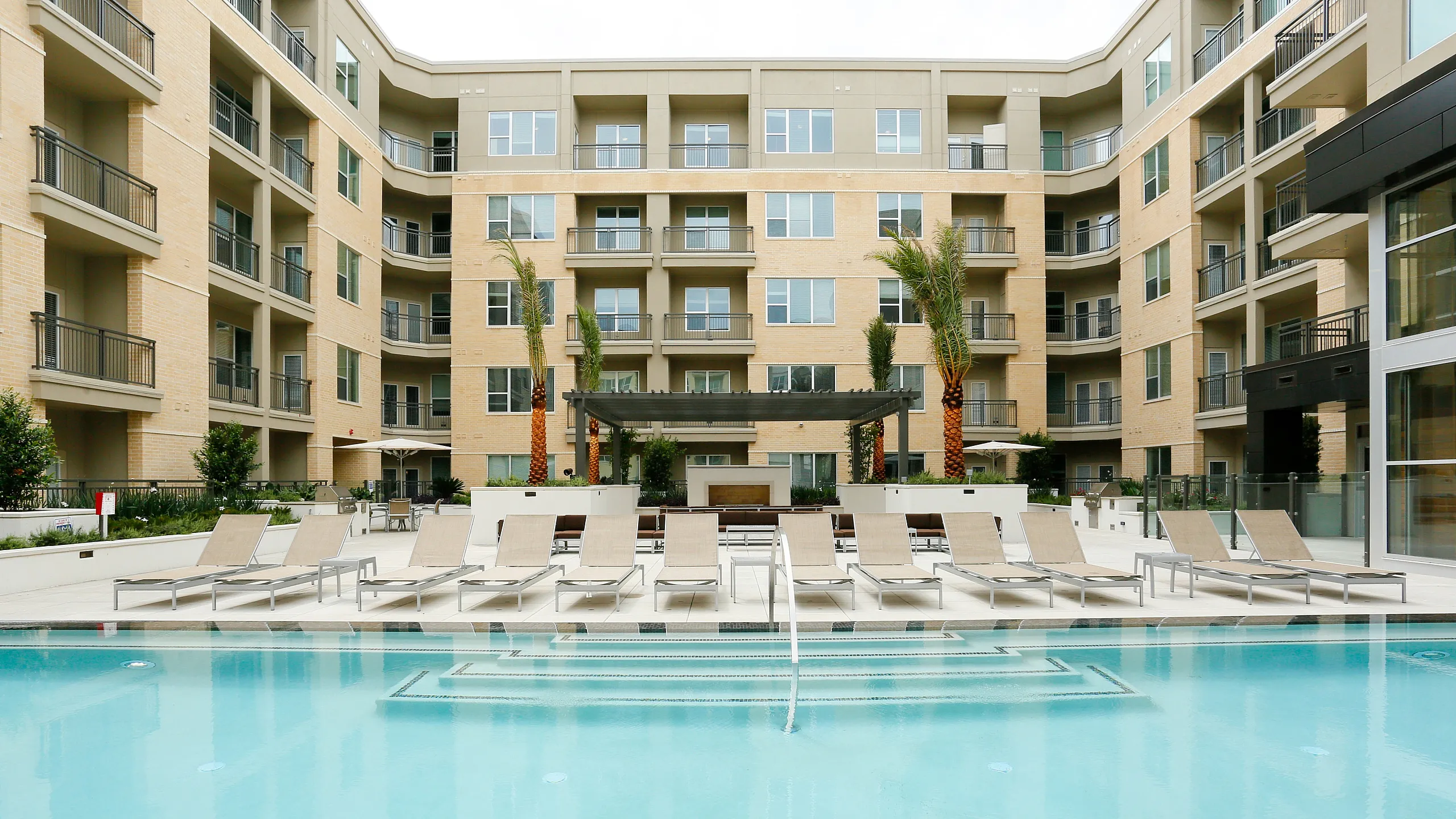 Luxurious apartment complex with a sparkling swimming pool and elegant poolside loungers, perfect for relaxation and leisure.
