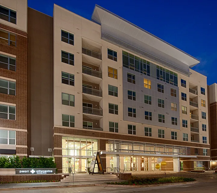 Modern urban apartment complex illuminated at night, showcasing contemporary architecture with brick and glass facade.
