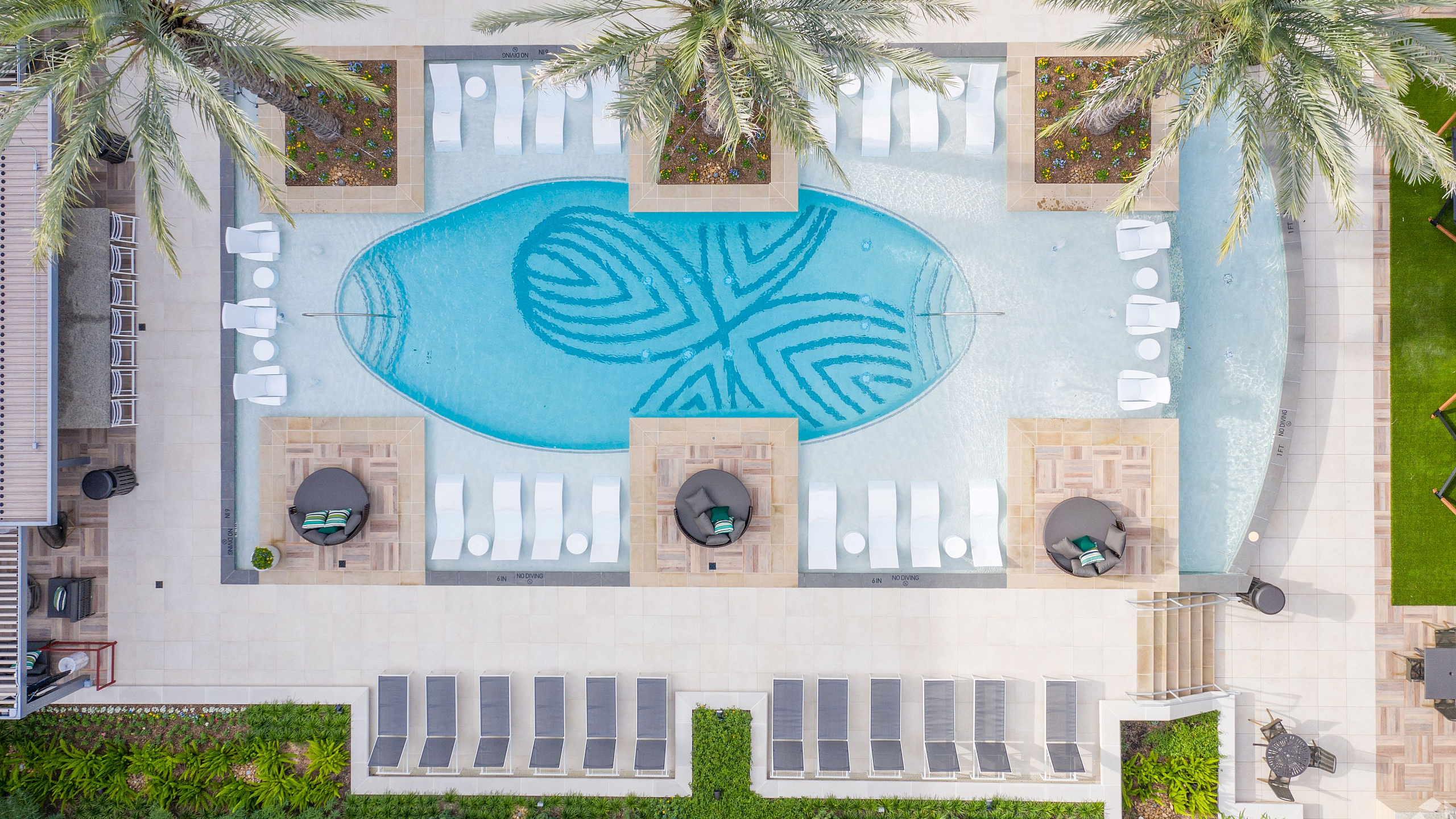 Luxurious aerial view of an elegant swimming pool surrounded by lush palm trees and stylish lounge chairs, offering a serene oasis for relaxation and rejuvenation.