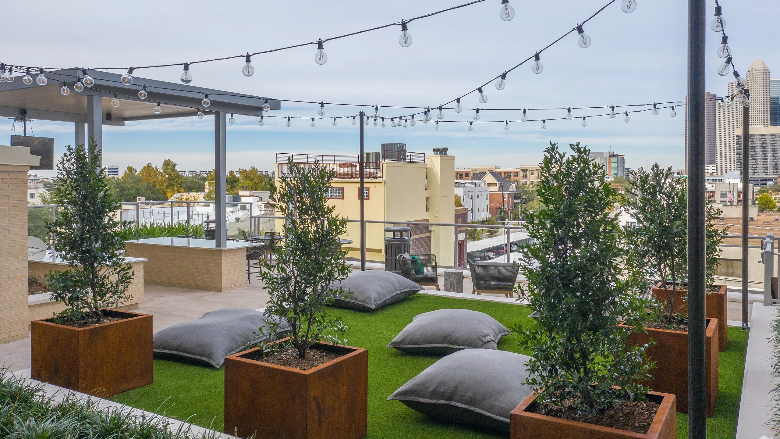 Chic rooftop terrace featuring lush green space, cozy seating, and string lights, with scenic city views.