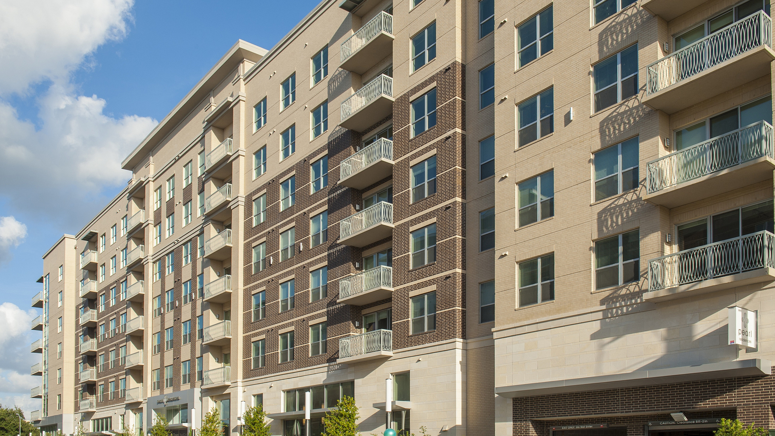 Contemporary urban apartment building with modern balconies and lush greenery, under a beautiful blue sky.