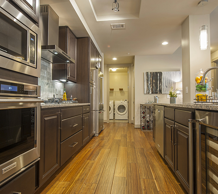 Elegant kitchen with sleek stainless steel appliances, rich wooden cabinetry, and modern lighting, leading to a cozy laundry room.
