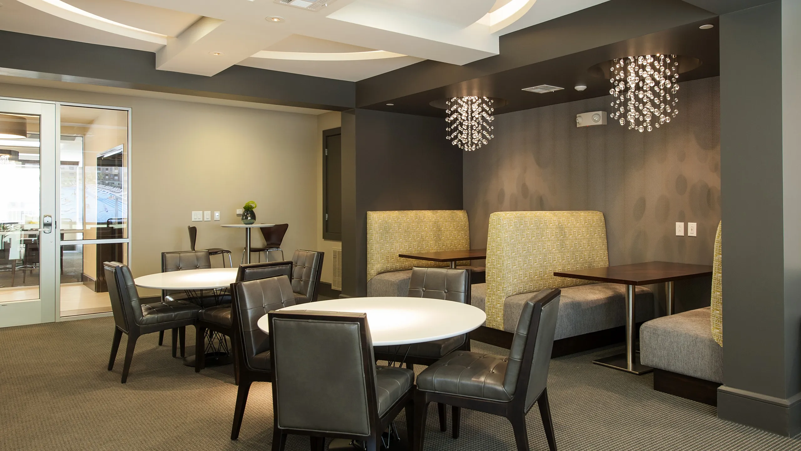 Elegant communal area with modern dining tables, stylish leather chairs, and cozy booth seating under chic crystal chandeliers, perfect for gatherings.