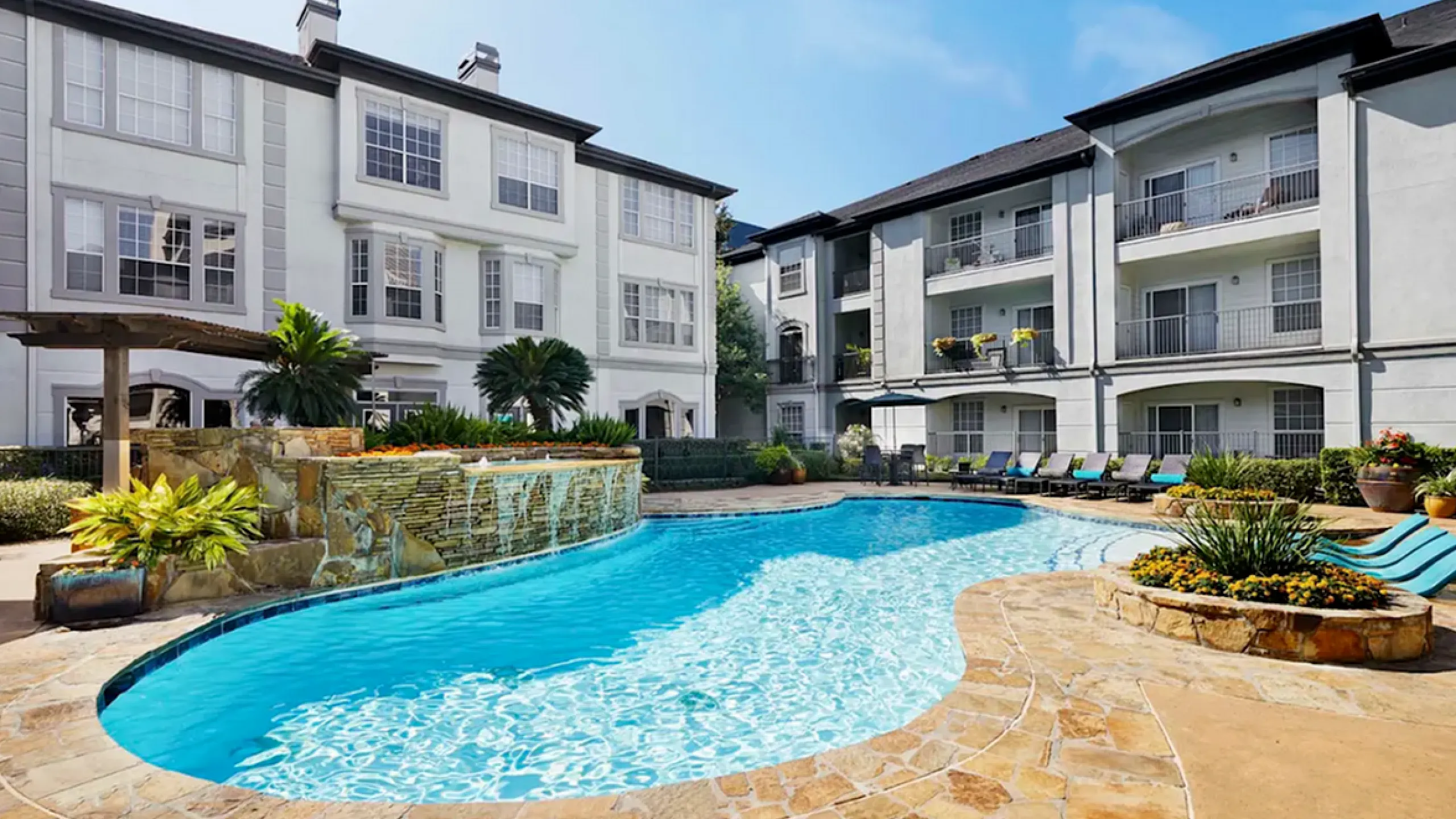Luxurious apartment complex with a stunning resort-style pool, surrounded by lush greenery and elegant architecture.