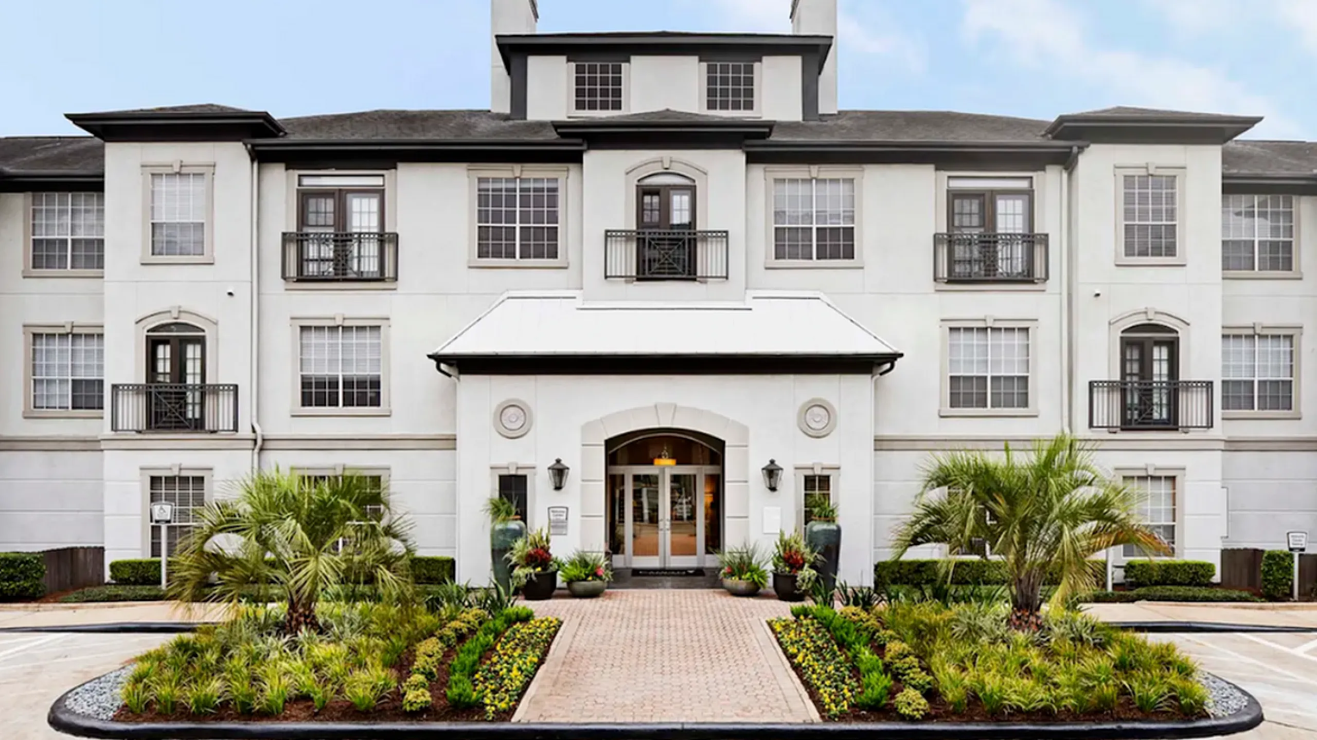 Elegant apartment building with classic architecture and lush landscaping, featuring large windows and a welcoming entrance.