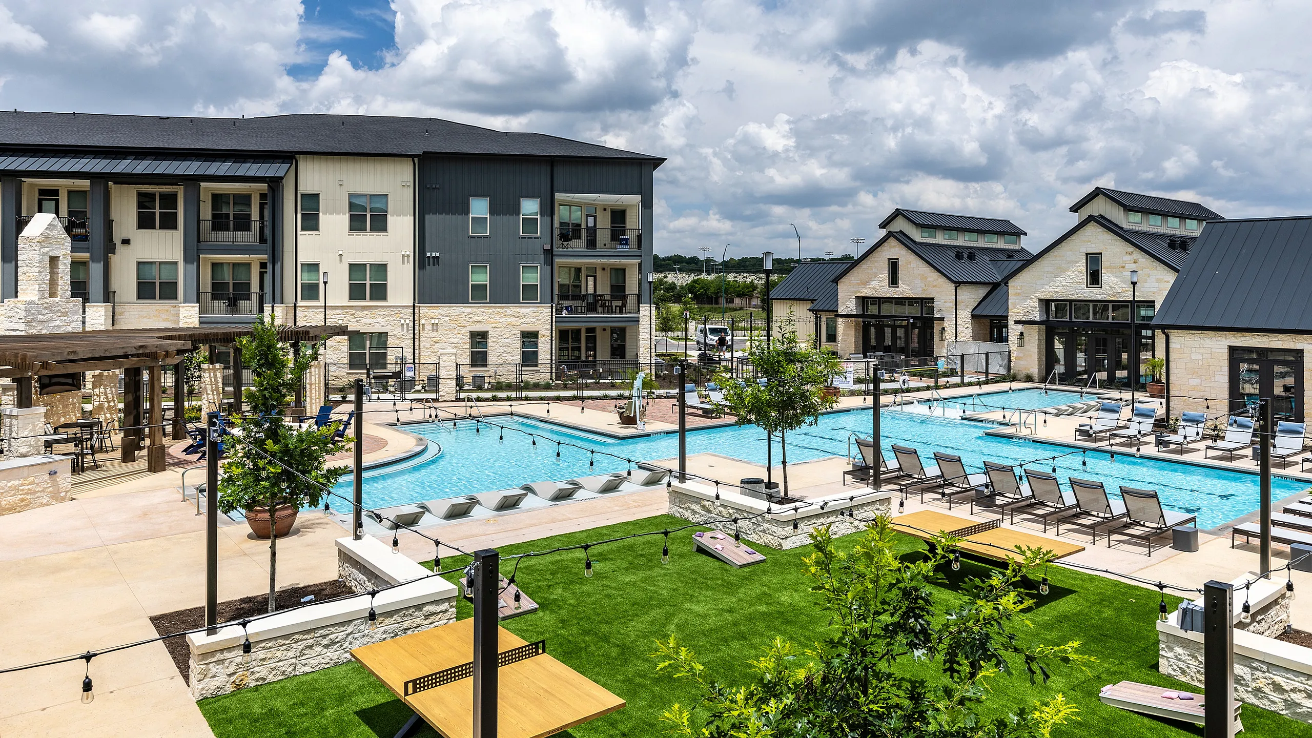 Luxurious apartment complex with a stunning outdoor pool, modern lounge chairs, and vibrant landscaped gardens under a bright blue sky.