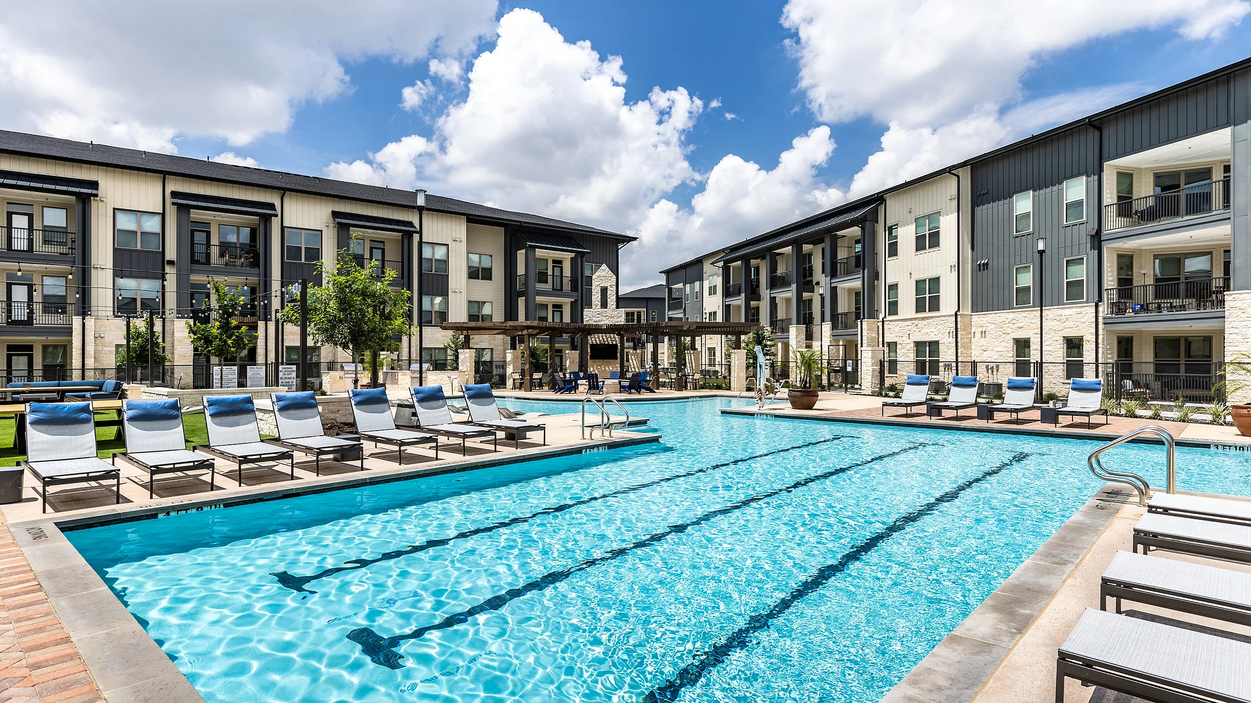 Luxurious apartment complex featuring a sparkling resort-style pool with modern lounge chairs and beautifully landscaped surroundings.