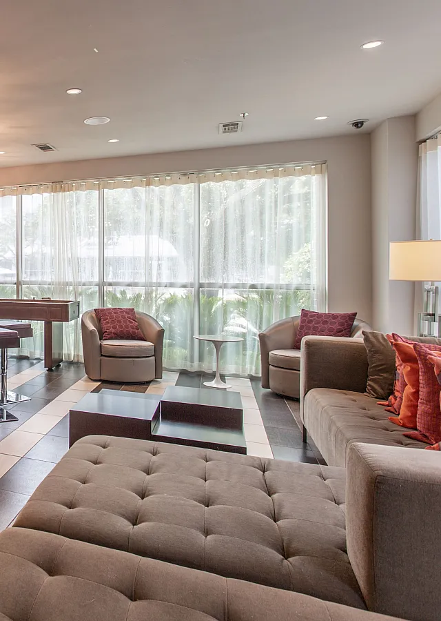 Elegant lounge area featuring a modern bar with sleek stools, plush seating, and stylish lighting, complemented by large windows and contemporary decor.