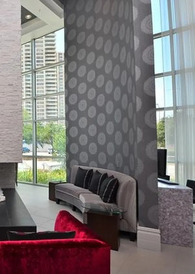 Luxurious apartment lobby with modern design features, tall windows offering city views, and chic furniture around a central fireplace.
