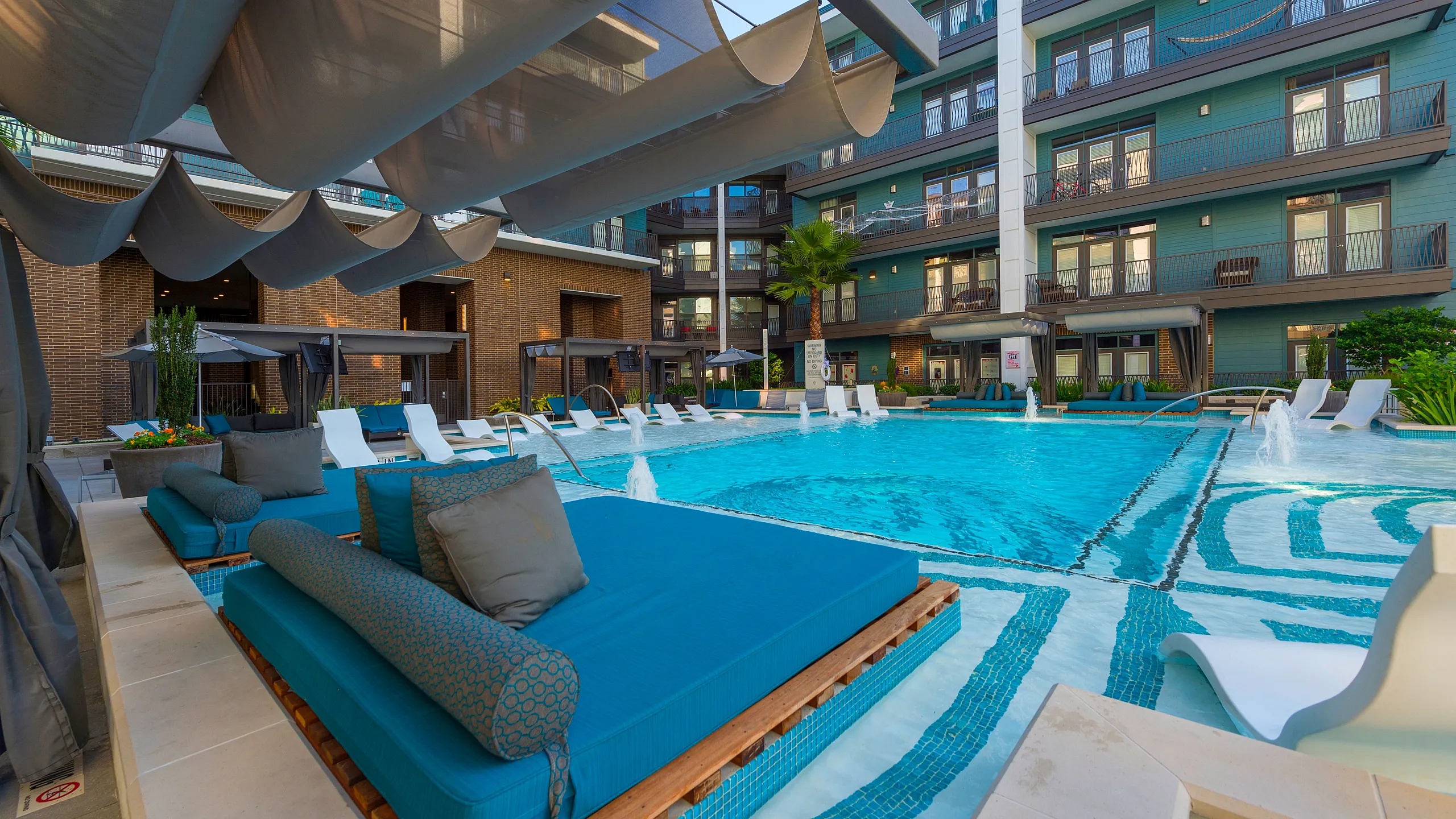 Luxurious apartment complex with a chic poolside lounge area featuring stylish blue daybeds, sleek modern architecture, and inviting swimming pool for relaxation and recreation.