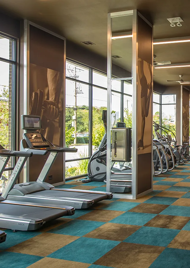 Modern fitness center with state-of-the-art cardio and strength training equipment, featuring large windows for natural light and vibrant checkered flooring.