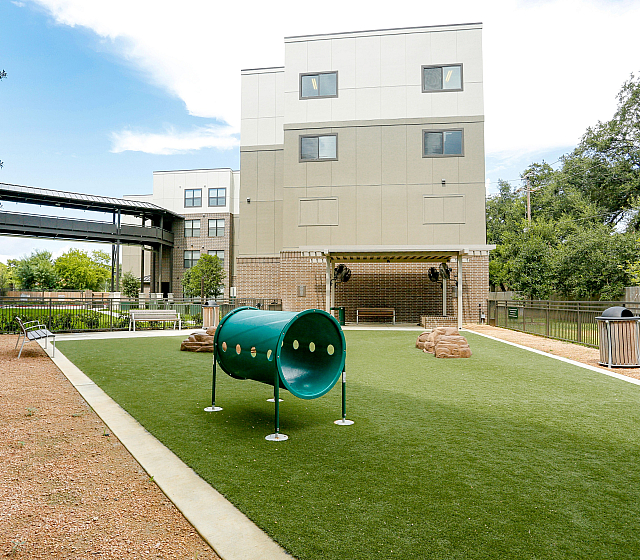 Inviting apartment complex with a well-maintained outdoor play area featuring a vibrant green tunnel and lush landscaping, perfect for relaxation and outdoor activities.