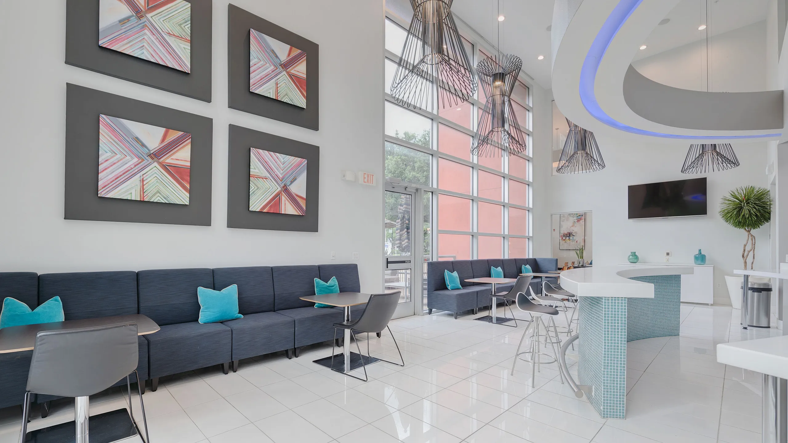 Bright and modern lobby area with stylish blue seating, artistic decor, floor-to-ceiling windows, and sleek overhead lighting.