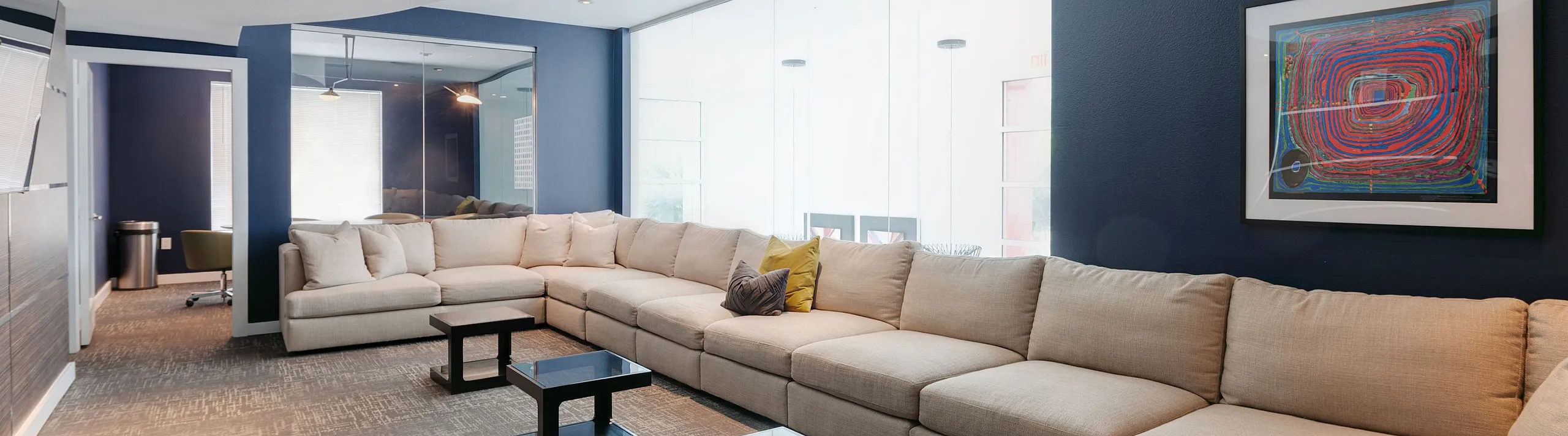 Modern and spacious lounge area with a stylish L-shaped beige sofa, elegant navy blue walls, and contemporary art accentuating the ambiance.