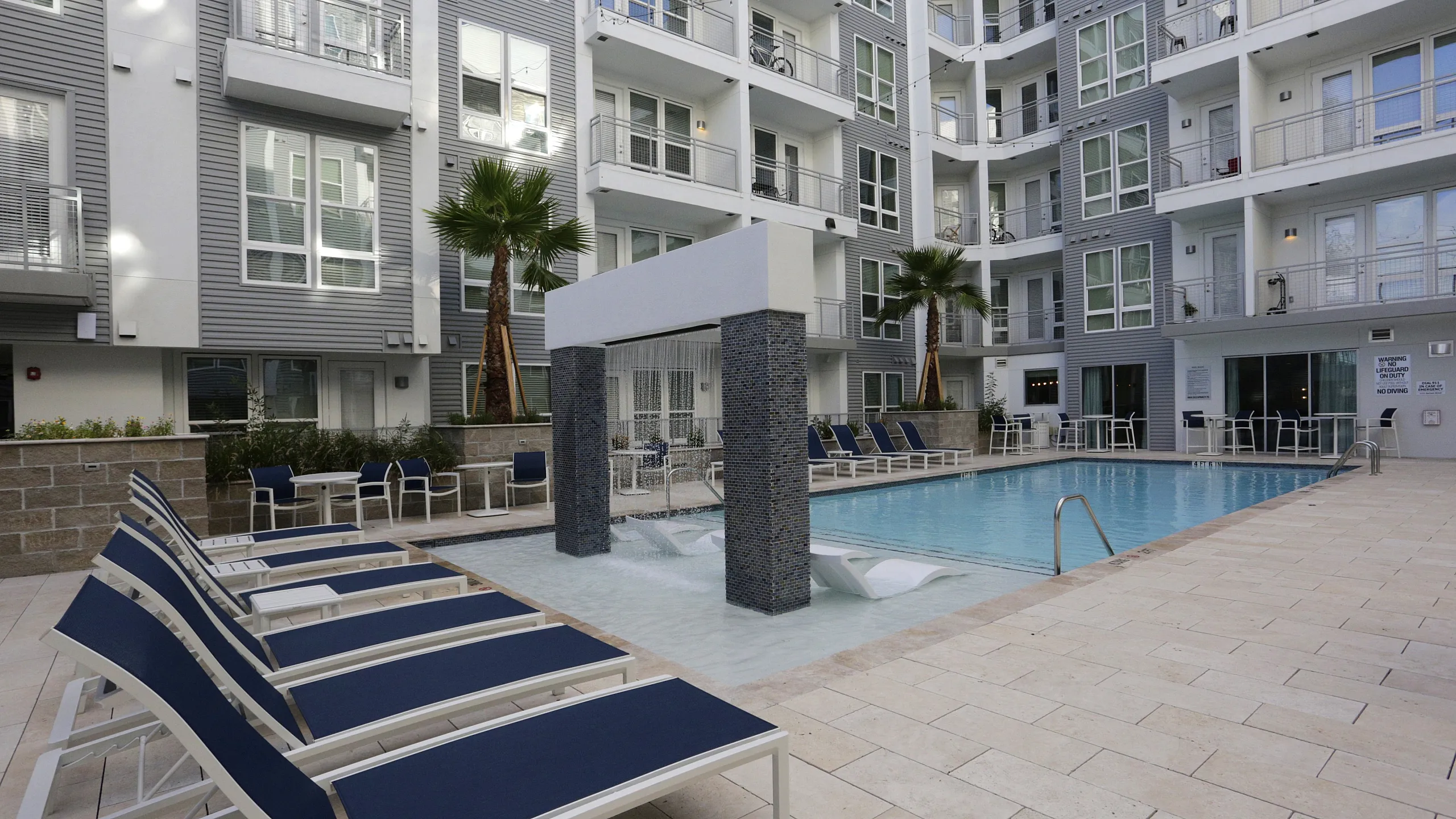 Modern apartment complex featuring a pristine outdoor pool area with sun loungers, chic water feature, and stylish seating for relaxation.