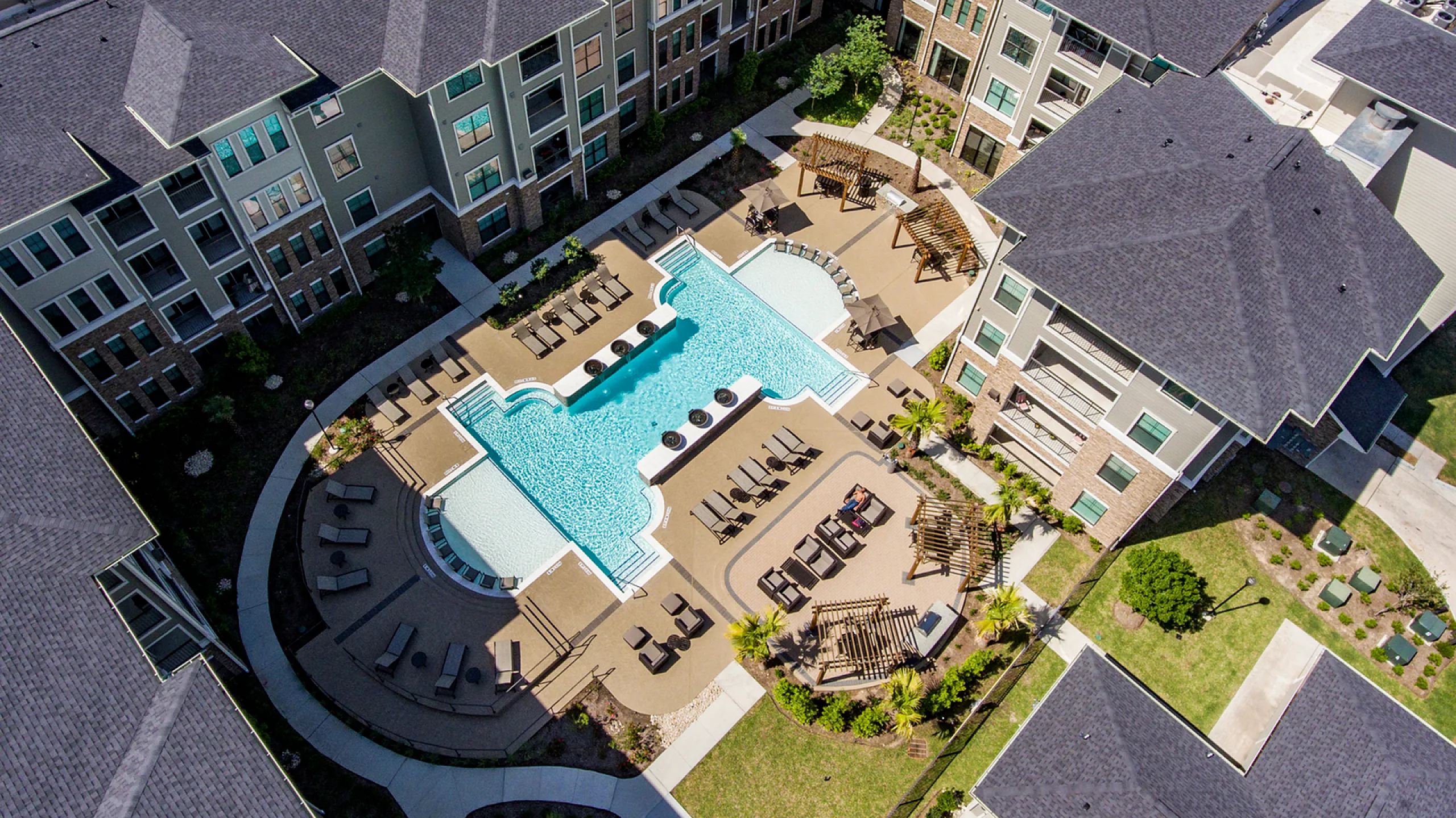 Luxurious apartment complex showcasing a stunning aerial view of a resort-style pool area surrounded by modern architecture and lush landscaping.