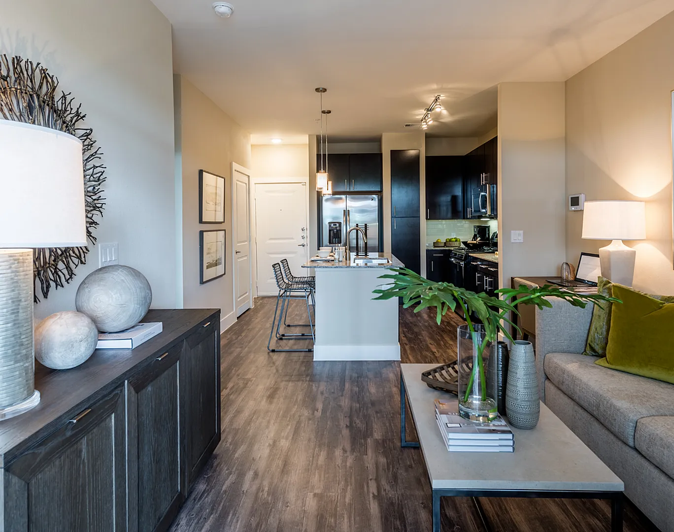 Chic modern apartment living room with stylish decor, comfortable grey sofa, sleek hardwood floors, and an open kitchen featuring stainless steel appliances.