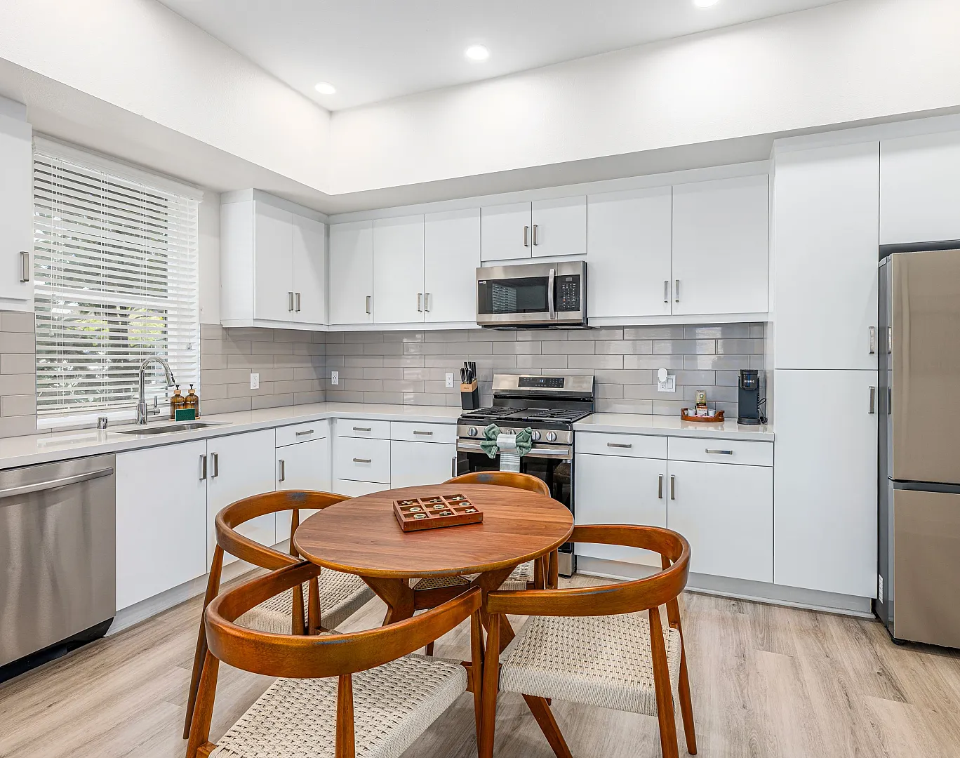 Modern kitchen with stainless steel appliances, sleek white cabinets, and a cozy wooden dining table for four.