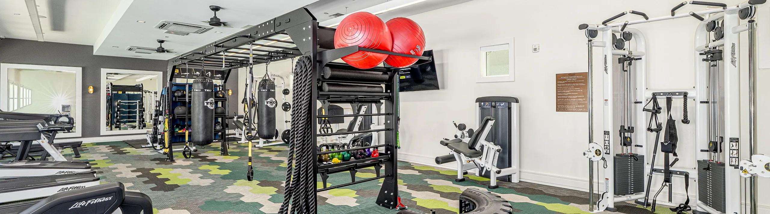 Modern fitness center with a variety of gym equipment, including treadmills, punching bags, and free weights, set on vibrant geometric flooring.