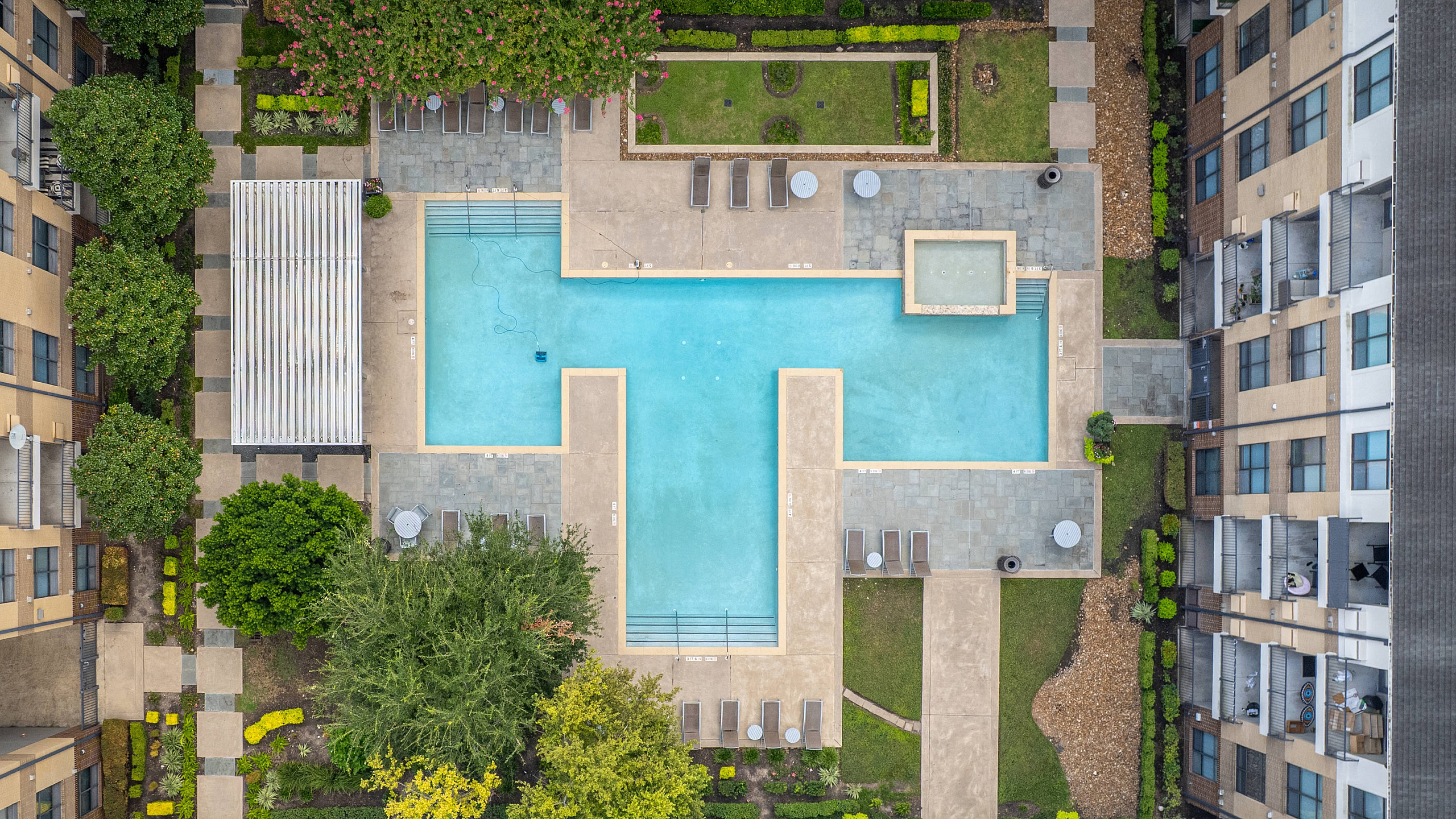 Elegant aerial view of luxury apartment complex featuring a large T-shaped swimming pool surrounded by lush greenery, lounge chairs, and modern architecture.