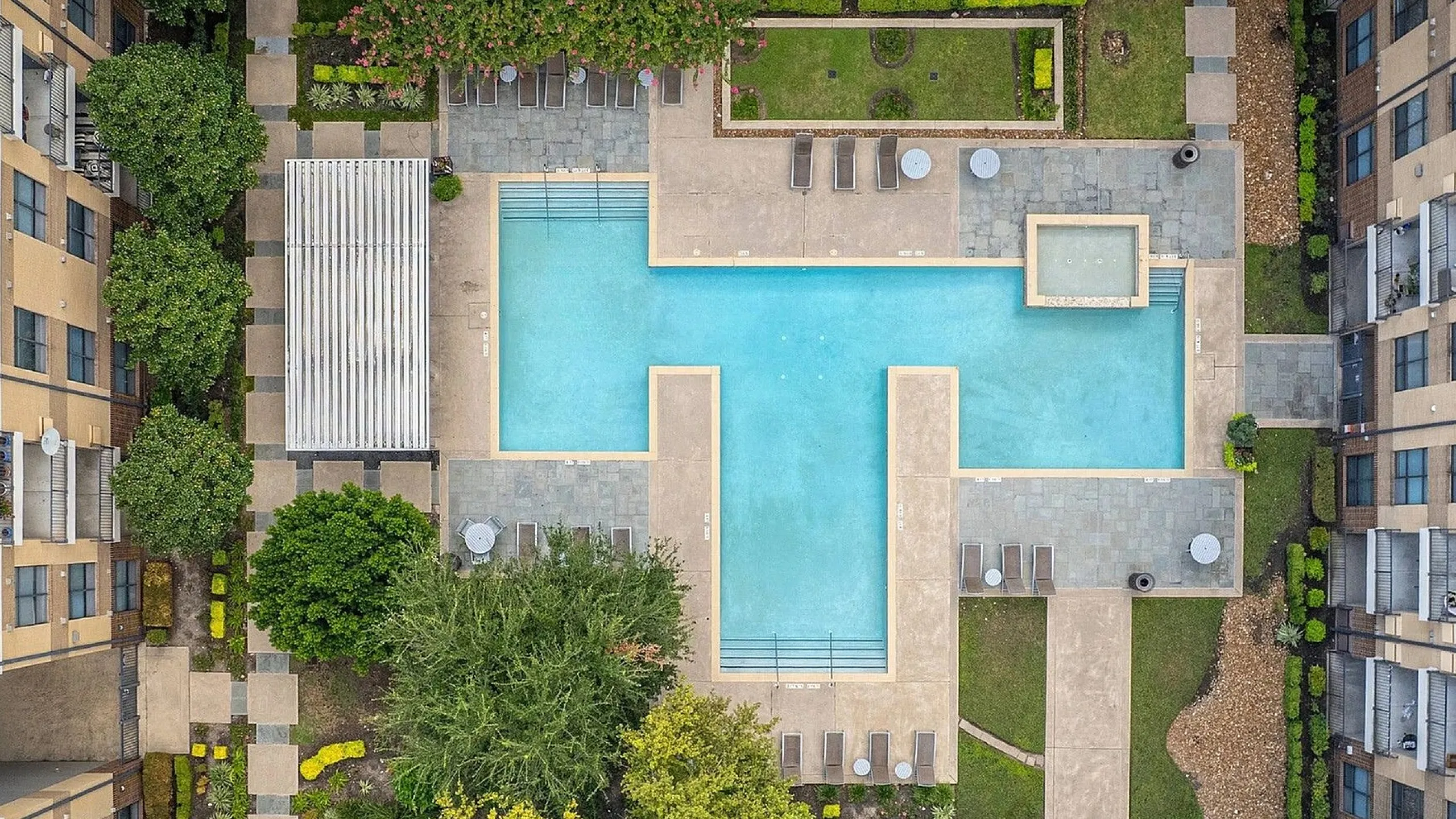 Stunning aerial view of a luxury apartment complex featuring a large, inviting swimming pool surrounded by lush greenery and stylish lounge areas.